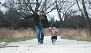 Father and daughter holding hands and running on a sidewalk