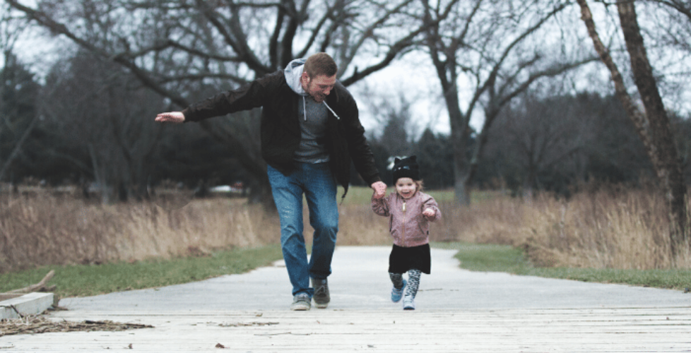 Father and daughter holding hands and running on a sidewalk